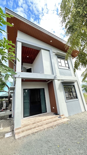 A modern two-story building with a flat roof, large windows, and a visible staircase leading to the entrance.