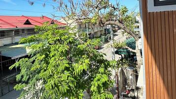 A balcony with a view of a red-roofed building, a tree, and a stone wall.