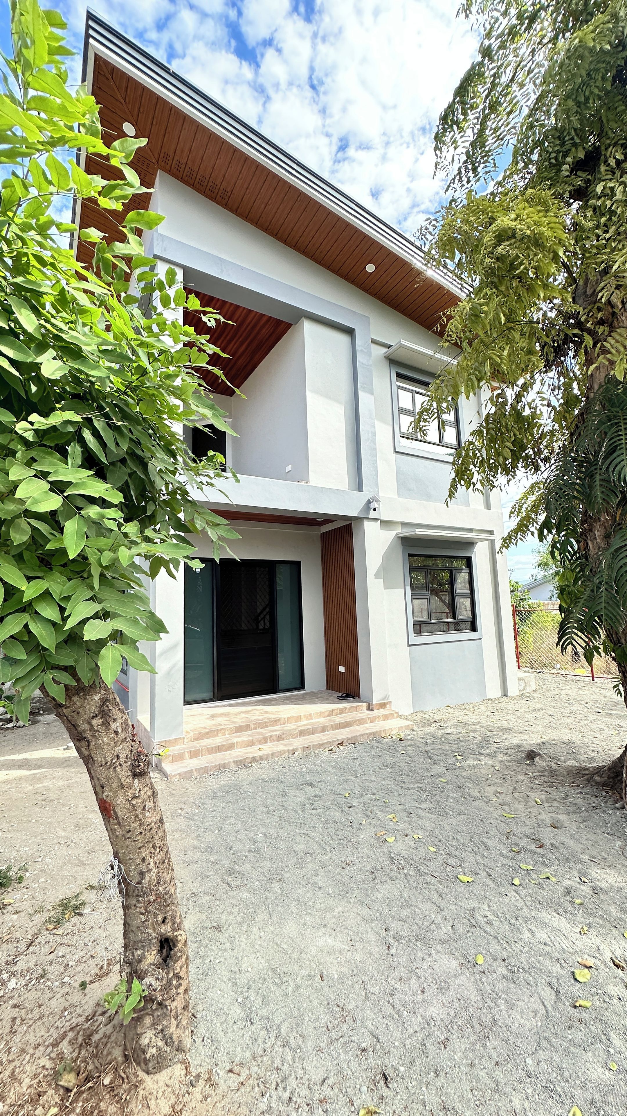 A modern two-story house with a flat roof, a front porch, and a gravel driveway.
