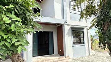 A modern two-story house with a flat roof, a front porch, and a gravel driveway.