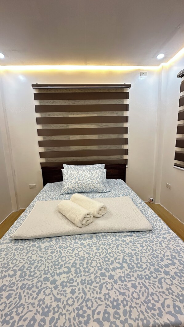 A neatly made bed with a patterned bedspread, a pillow, and two folded towels.