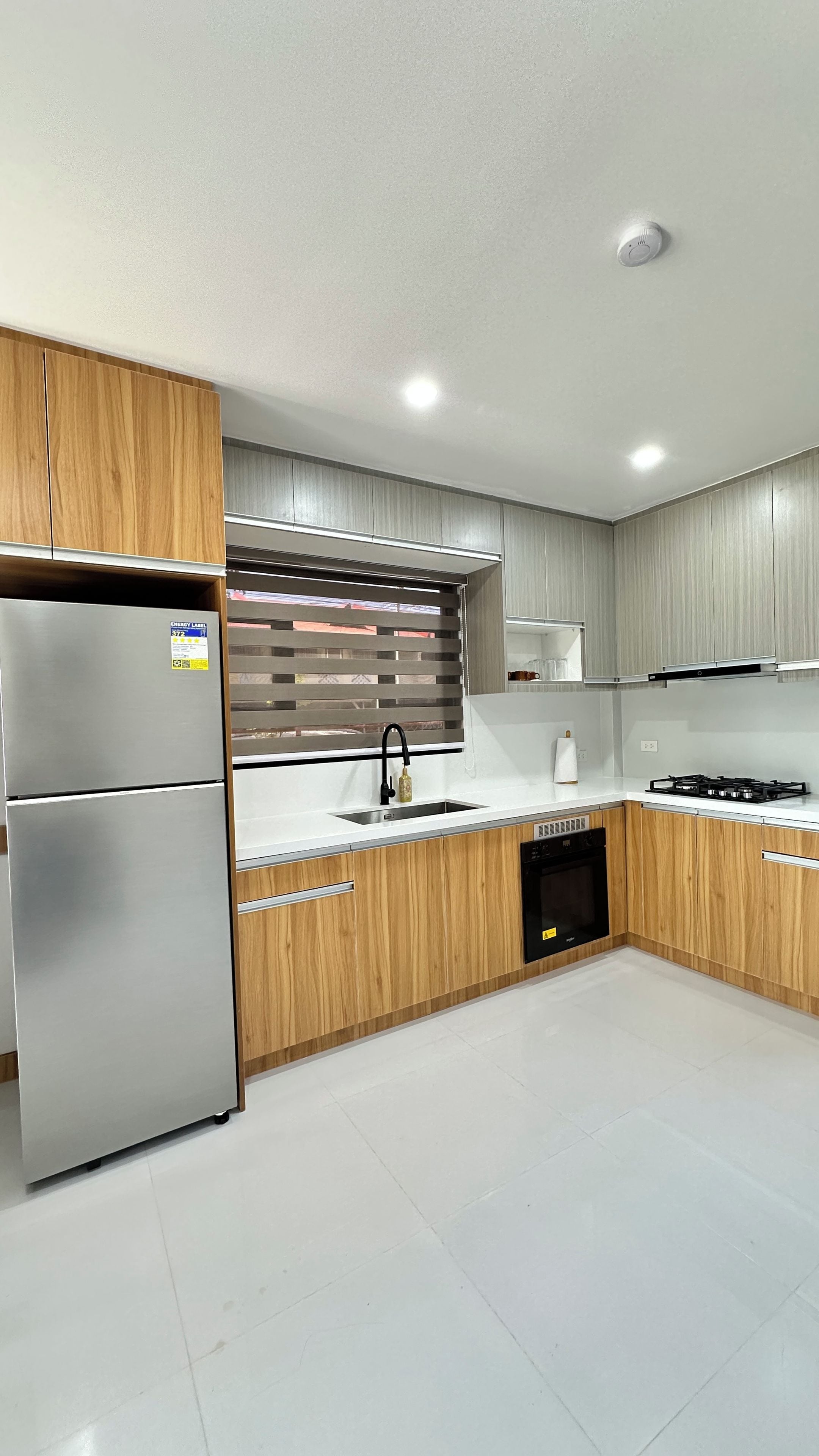 A modern kitchen with a stainless steel refrigerator, wooden cabinets, a built-in oven, and a dishwasher.