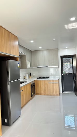 A modern kitchen with stainless steel appliances, wooden cabinets, and a black door.