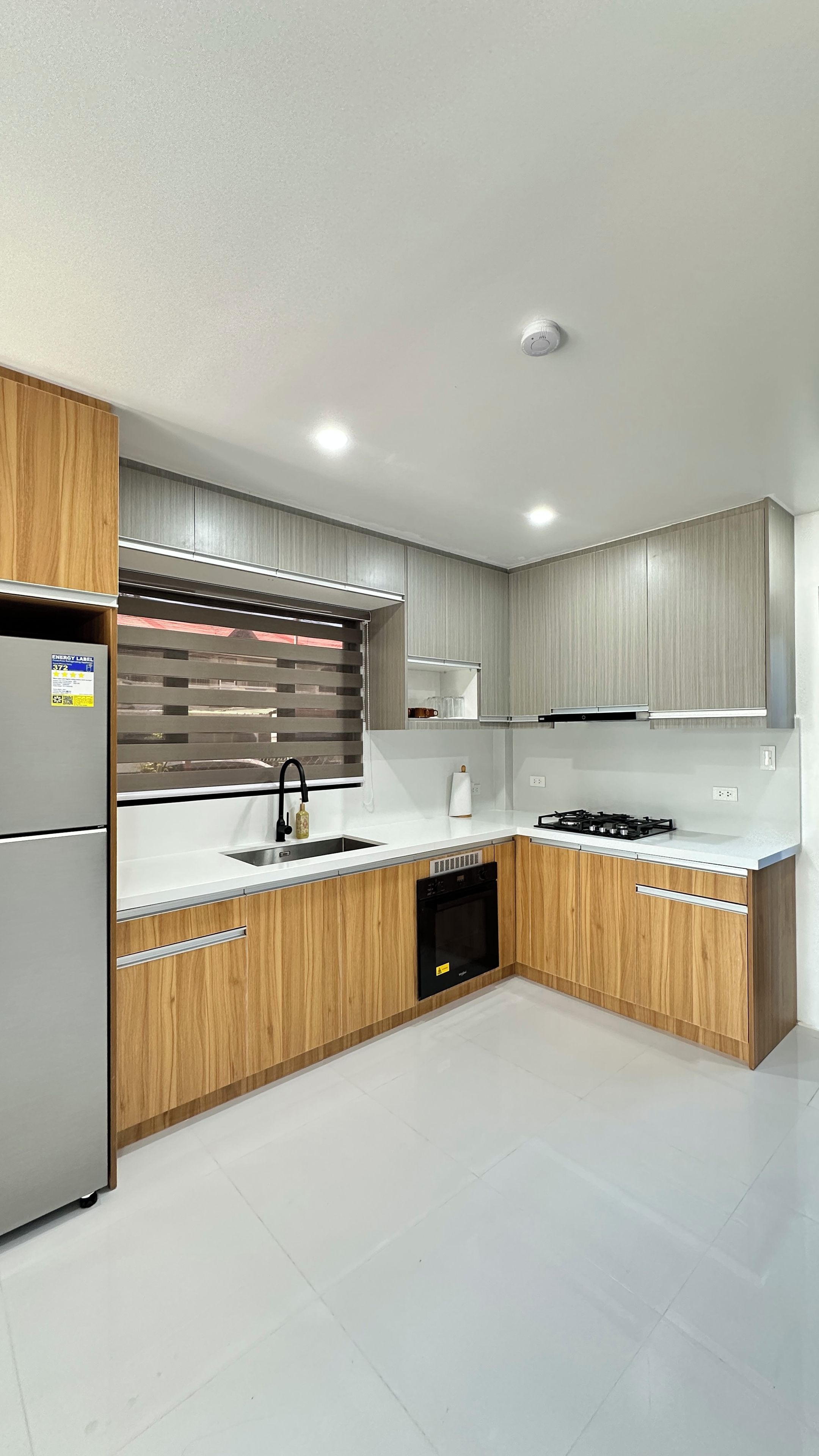 A modern kitchen with wooden cabinetry, a stainless steel refrigerator, a built-in oven, and a gas stove.
