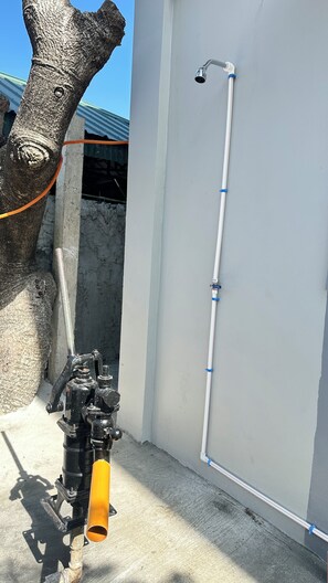 A water spigot attached to a concrete wall, a metal pipe, and a tree trunk.