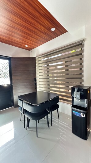 A modern kitchen with a wooden ceiling, a black dining table with chairs, a window with blinds, and a trash bin.