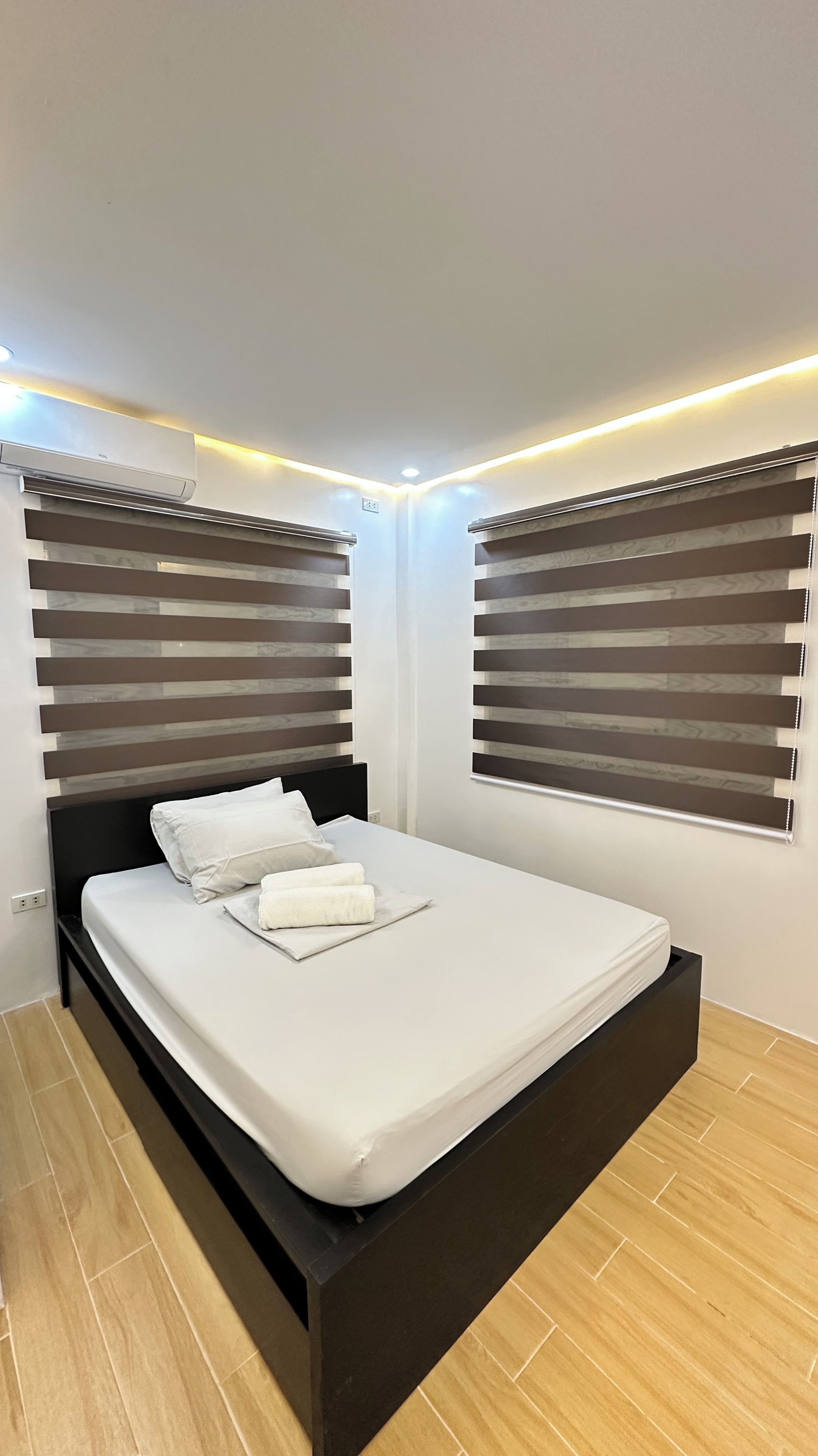 A modern bedroom with a black bed frame, white bedding, and wooden flooring.