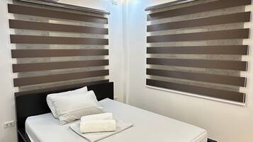 A modern bedroom with a black bed frame, white bedding, and wooden flooring.