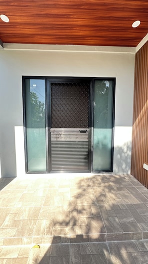 A modern entrance with a sliding glass door, a metal mesh screen, and a tiled patio area.