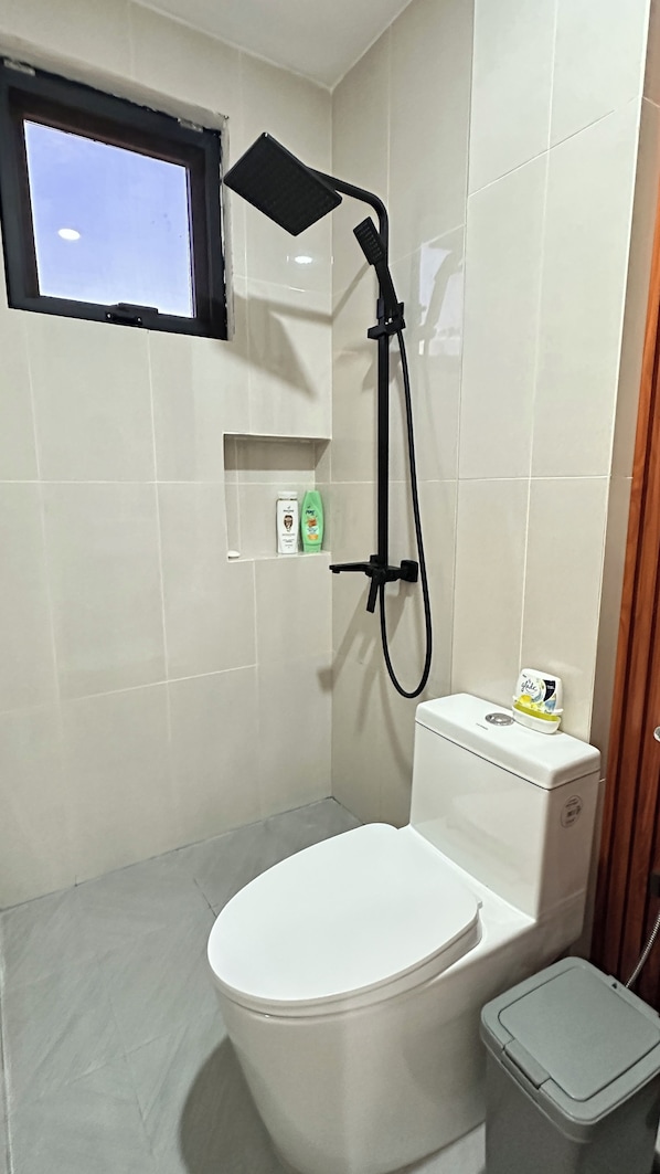 A bathroom with a white toilet, a showerhead, and a window.