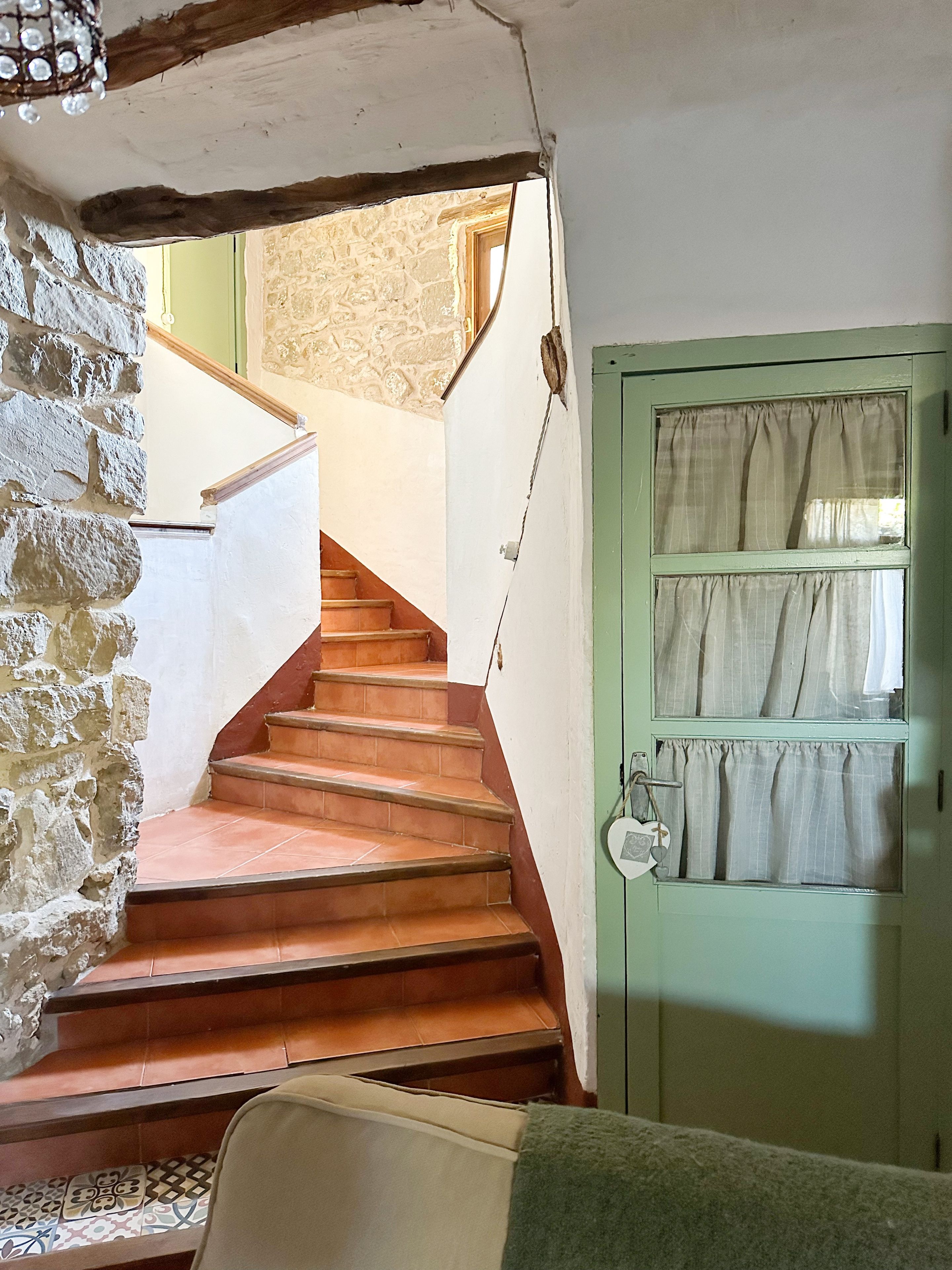Una escalera con paredes de piedra y una puerta verde con cortinas.