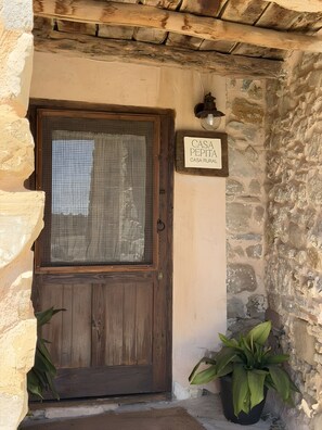 Une porte en bois rustique, dotée d’une moustiquaire, avec une enseigne au-dessus et un pot de fleurs placé à côté.