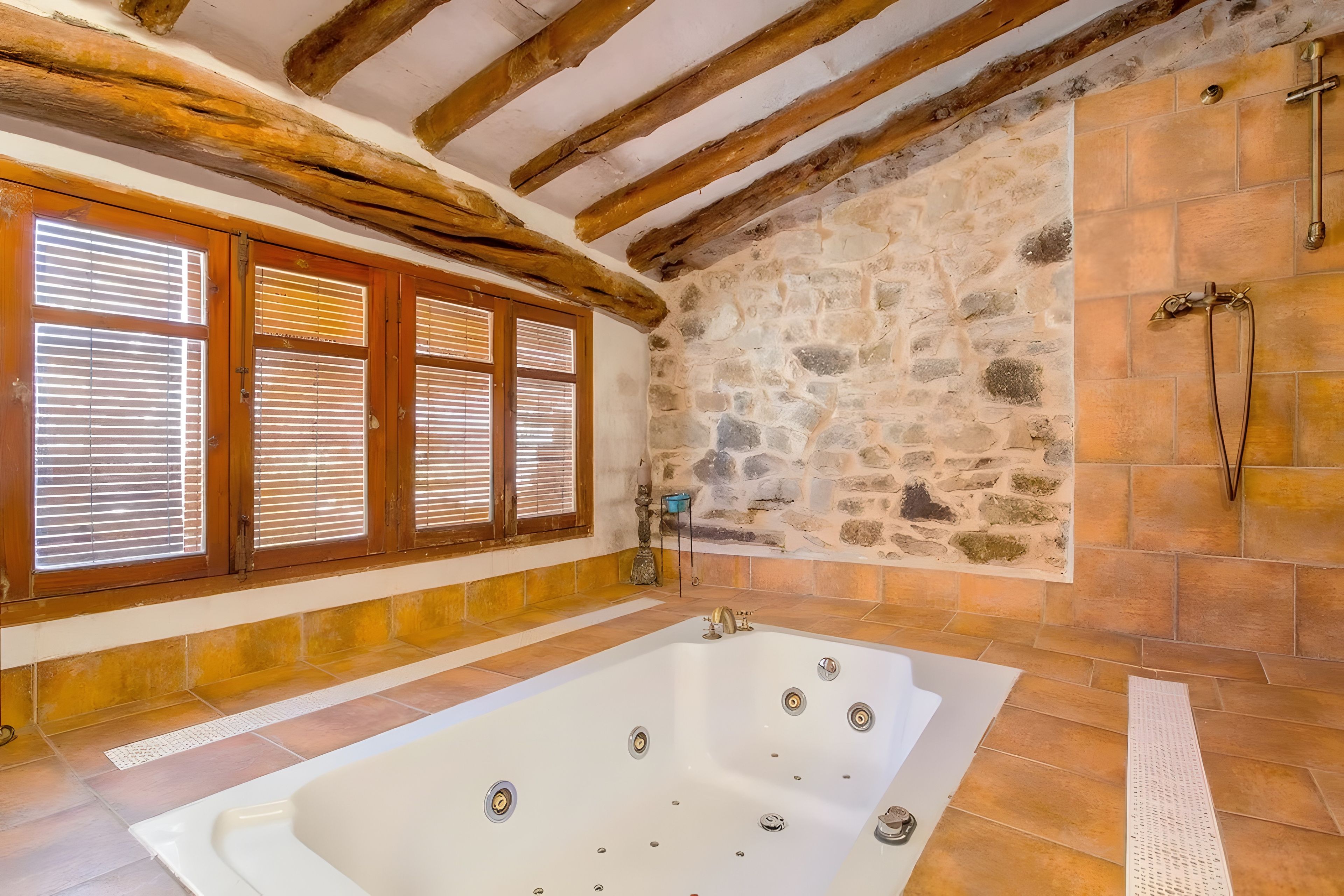 Un baño con pared de piedra, vigas de madera y una bañera.