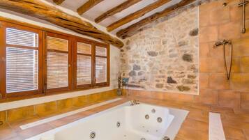 Un baño con pared de piedra, vigas de madera y una bañera.