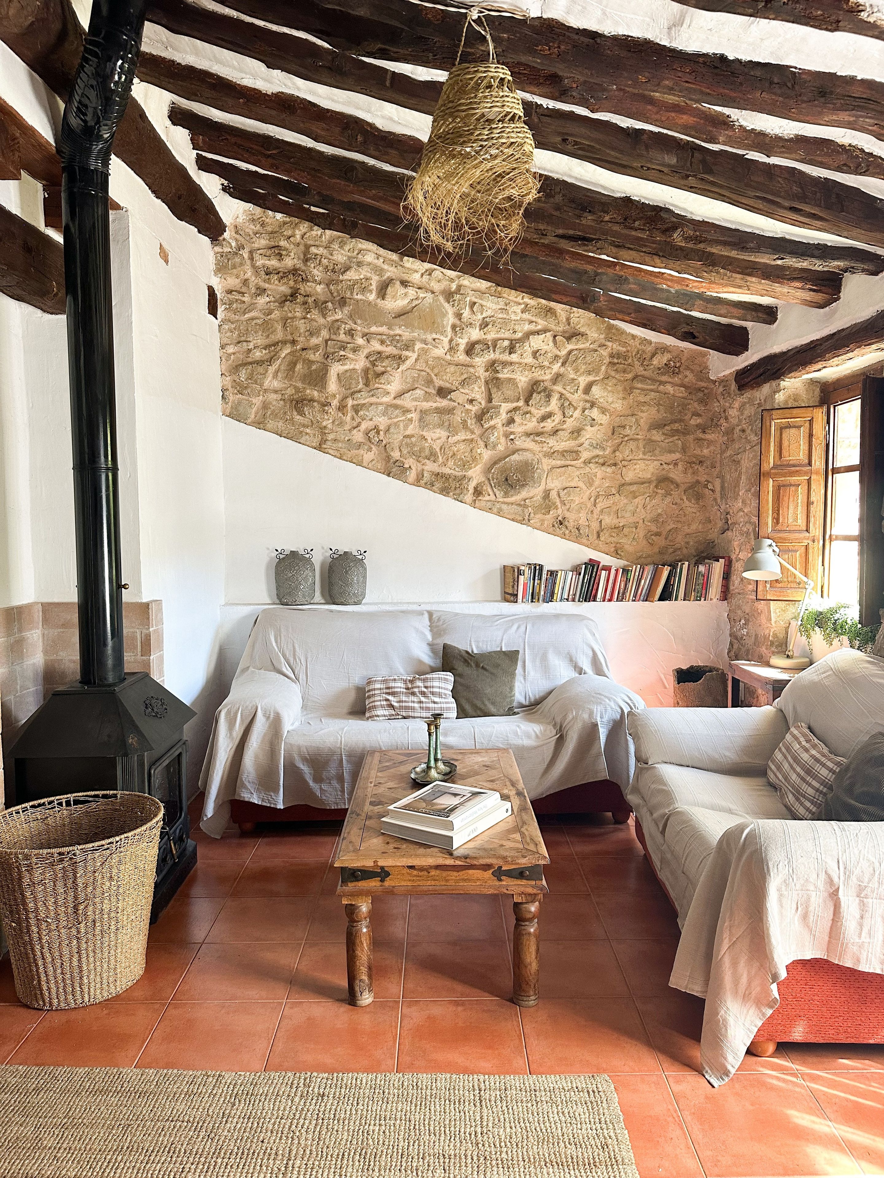 Una sala de estar rústica con pared de piedra, chimenea, sofá, mesa de centro y lámpara colgante.