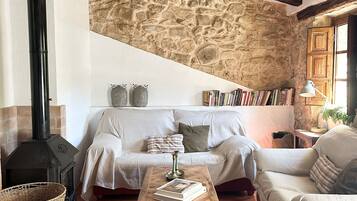 Una sala de estar rústica con pared de piedra, chimenea, sofá, mesa de centro y lámpara colgante.