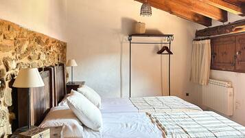 A bedroom with a wooden ceiling, stone wall, a bed with white bedding, a bedside table with a lamp, and a hanging light fixture.