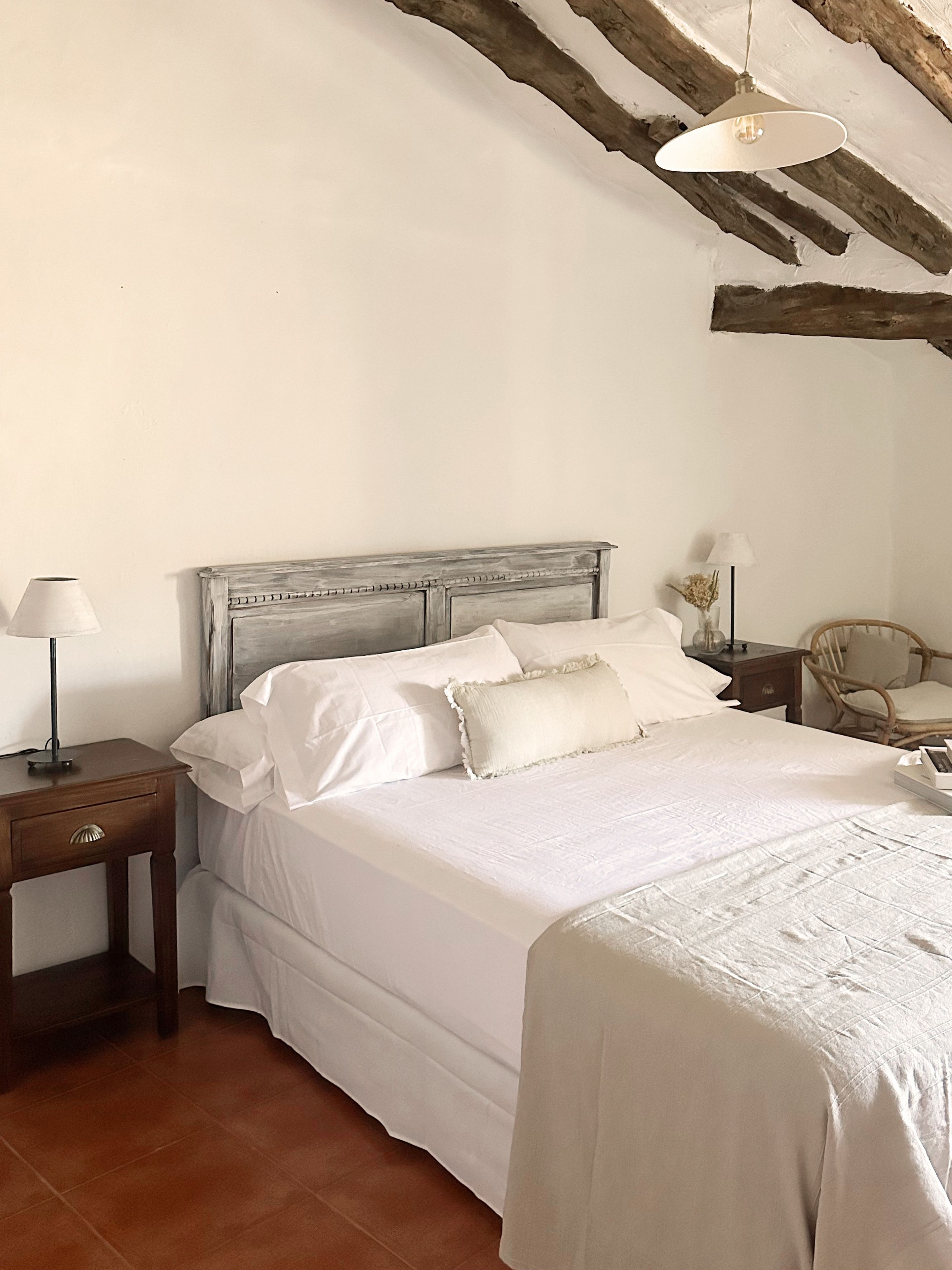 Una camera da letto con un letto, comodini, una sedia e una lampada a sospensione.