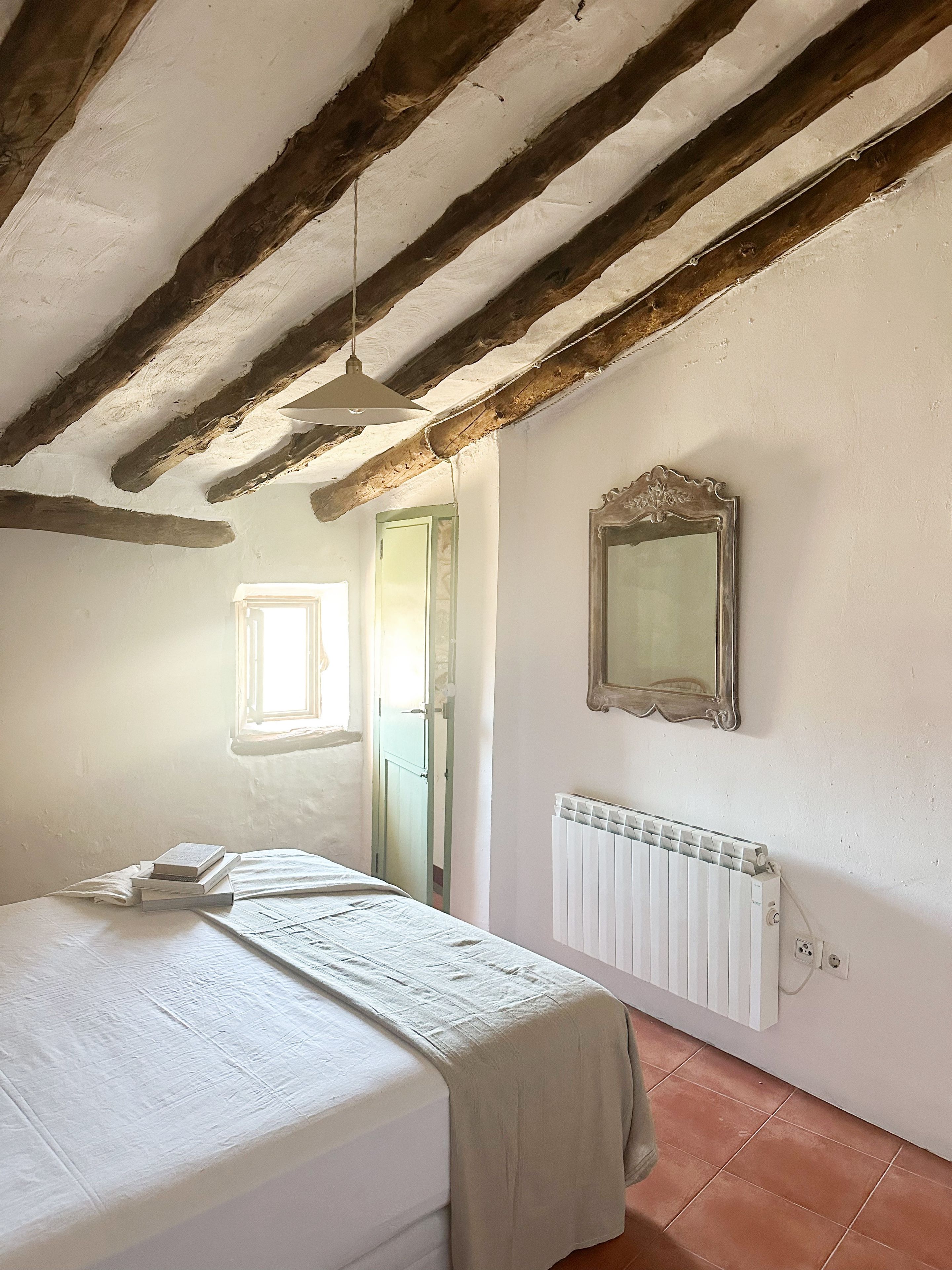 Een slaapkamer met een bed, een radiator, een spiegel en een raam.