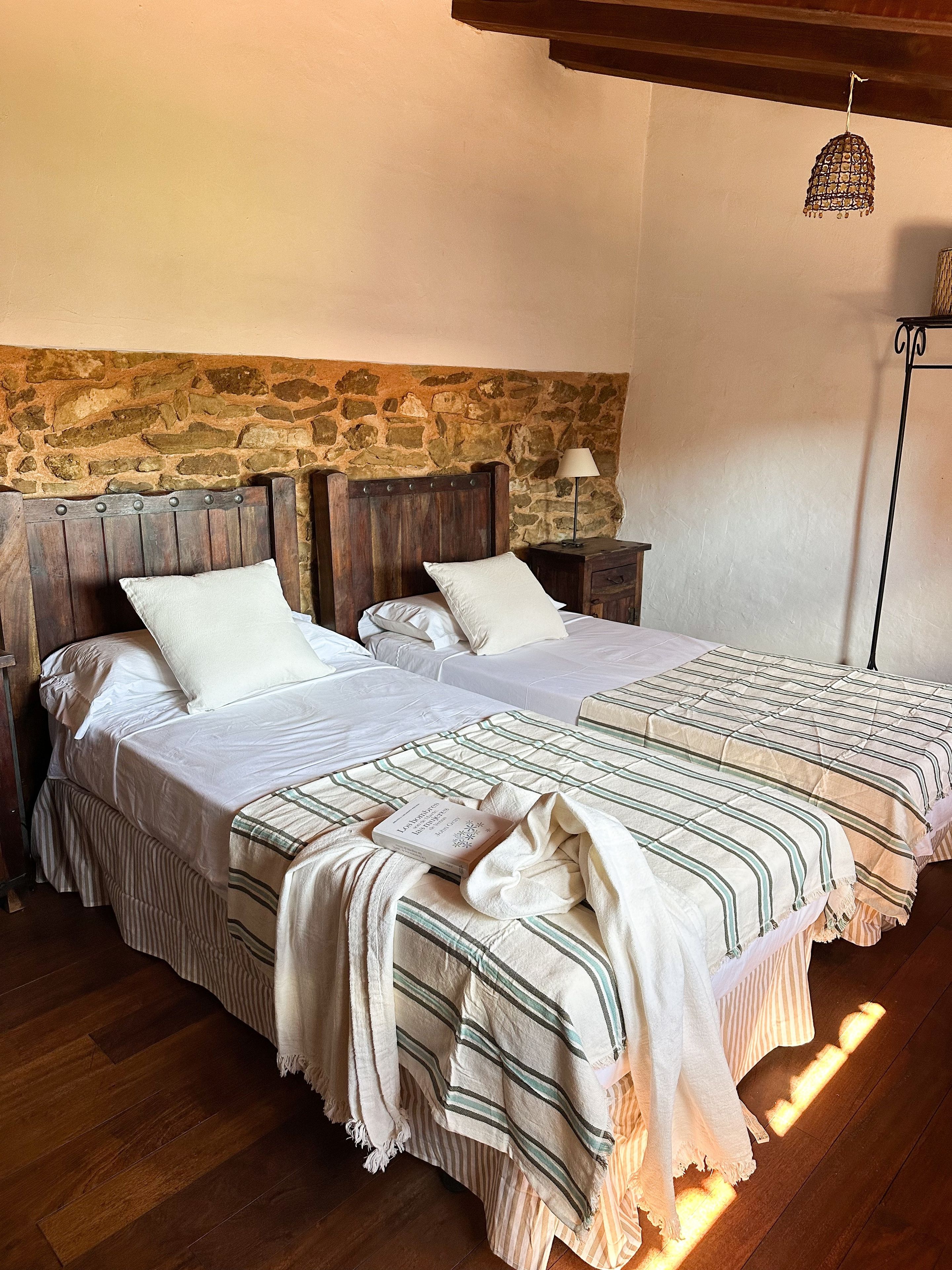 Una cama doble con una colcha a rayas, una mesita de noche con una lámpara y una pared de piedra al fondo.