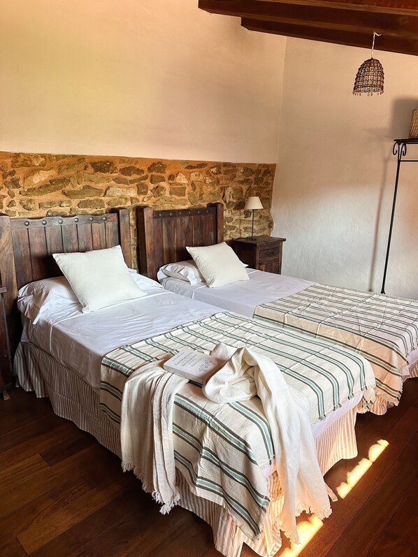 Un lit double avec une couverture à rayures, une table de chevet avec une lampe et un mur en pierre en arrière-plan.