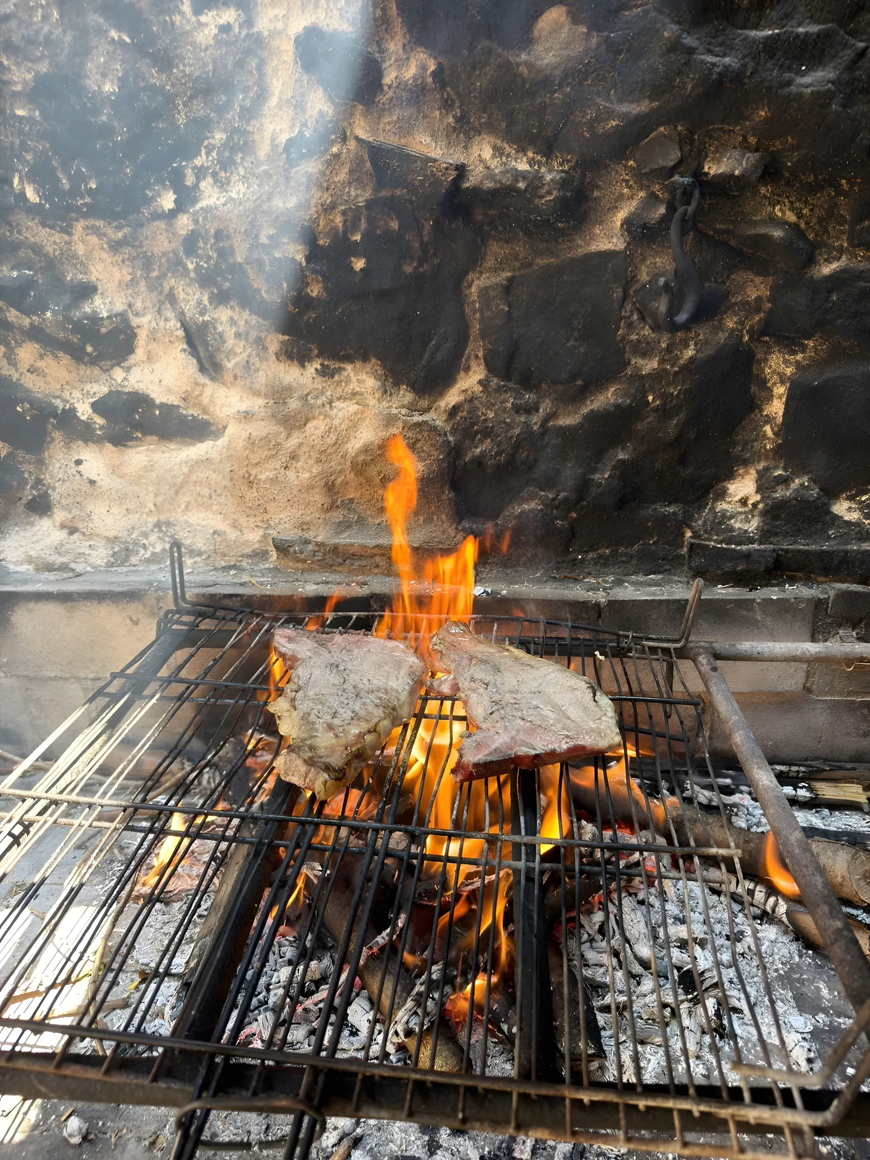 Una parrilla con dos filetes cocinándose sobre llamas abiertas.