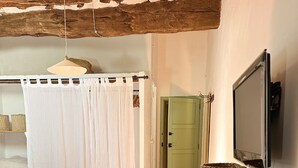 Quarto com cama, mesa de madeira com livros, porta verde e cortina branca.