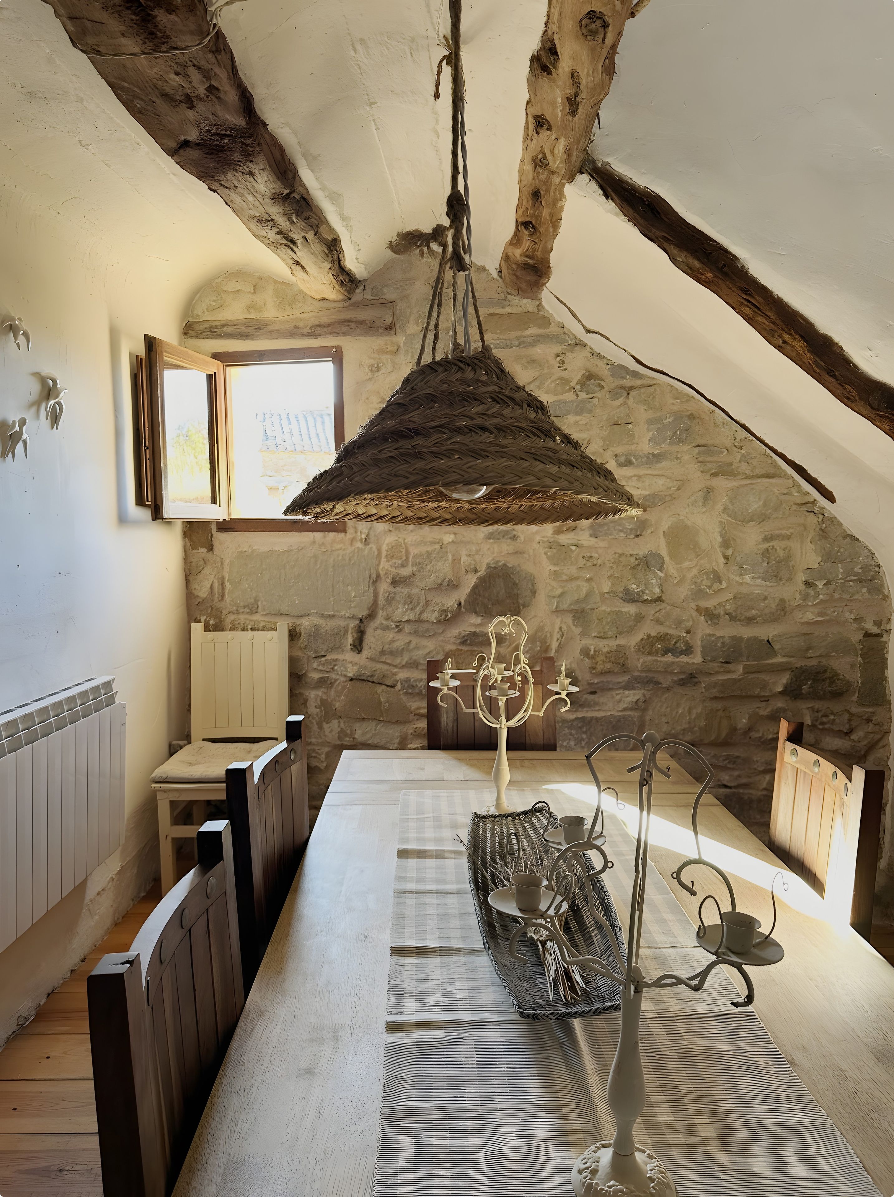 Une pièce rustique avec un mur en pierre, une table en bois sur laquelle repose un panier tressé, un chandelier et un luminaire suspendu.