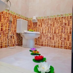 A bathroom with a toilet, a shower, and decorative lotus flowers on the floor. - Happy Holidays Hotel (Patong)