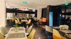 Een modern restaurant met verschillende eetgedeeltes, waaronder een bar/lounge met zitplaatsen en een apart dinergedeelte met tafels en stoelen.