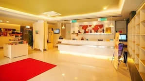 A hotel reception area with a white reception desk, a red carpet, and a modern interior design. - Magnolia Hotel (Wuxi)