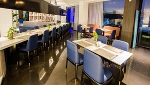 A modern hotel dining area with multiple tables and chairs, a bar area, and a view of the cityscape. - Magnolia Hotel (Wuxi)