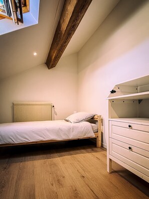 Une chambre à coucher avec un lit, une commode, un radiateur et un plafond en pente.