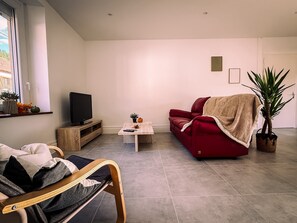 A modern living room with a red sofa, a television on a wooden stand, a coffee table, and a potted plant. - Family-Friendly Village House - LA PERLA (Éloyes)