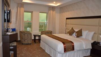 A hotel room with a large bed, a desk, a chair, a small table, and a window with curtains.