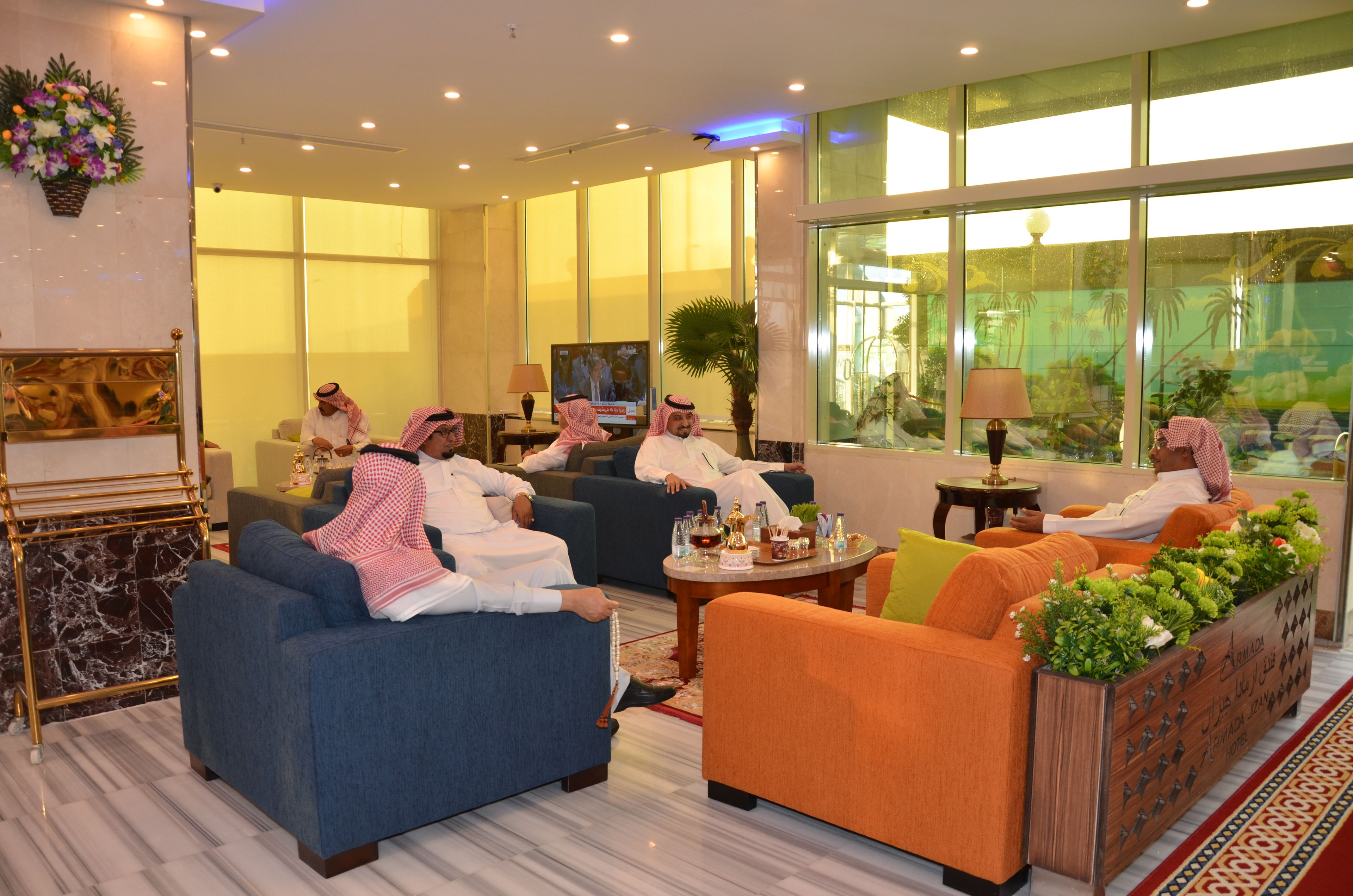A hotel lobby with multiple seating areas, a television, and a large window with a view of palm trees.
