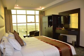A hotel room with a large bed, a desk, a chair, a wardrobe, and a TV. - Golden New Armada (Jizan)