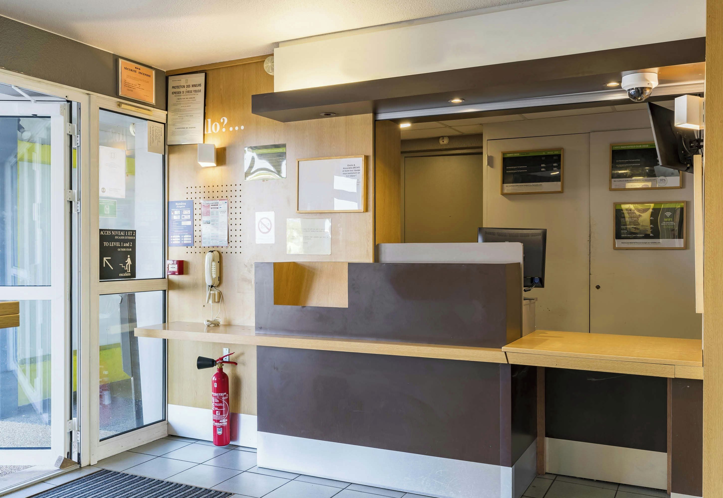 A reception desk with a fire extinguisher, a telephone, and various informational posters on the wall.