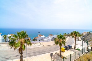 A coastal street with white buildings, palm trees, and a clear view of the sea. - Luxury Apartment in Torrox Costa (Torrox)