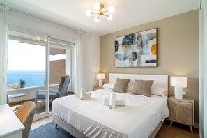 A hotel room with a bed, two bedside lamps, a painting, a view of the sea, and a balcony with a chair. - Luxury Apartment in Torrox Costa (Torrox)