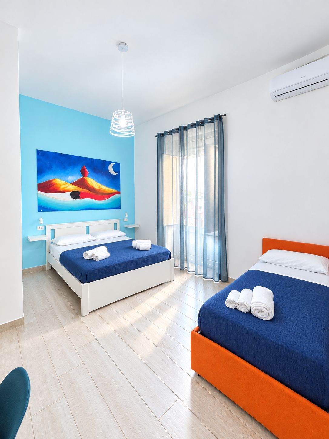 Une chambre d’hôtel avec deux lits, un tableau au mur, une fenêtre avec des rideaux et un appareil de climatisation.