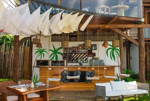 An outdoor bar area with wooden furniture, hanging white fabrics, and a wooden counter with a bar. - RCH Luxury Hotel & Pool (Dibulla)