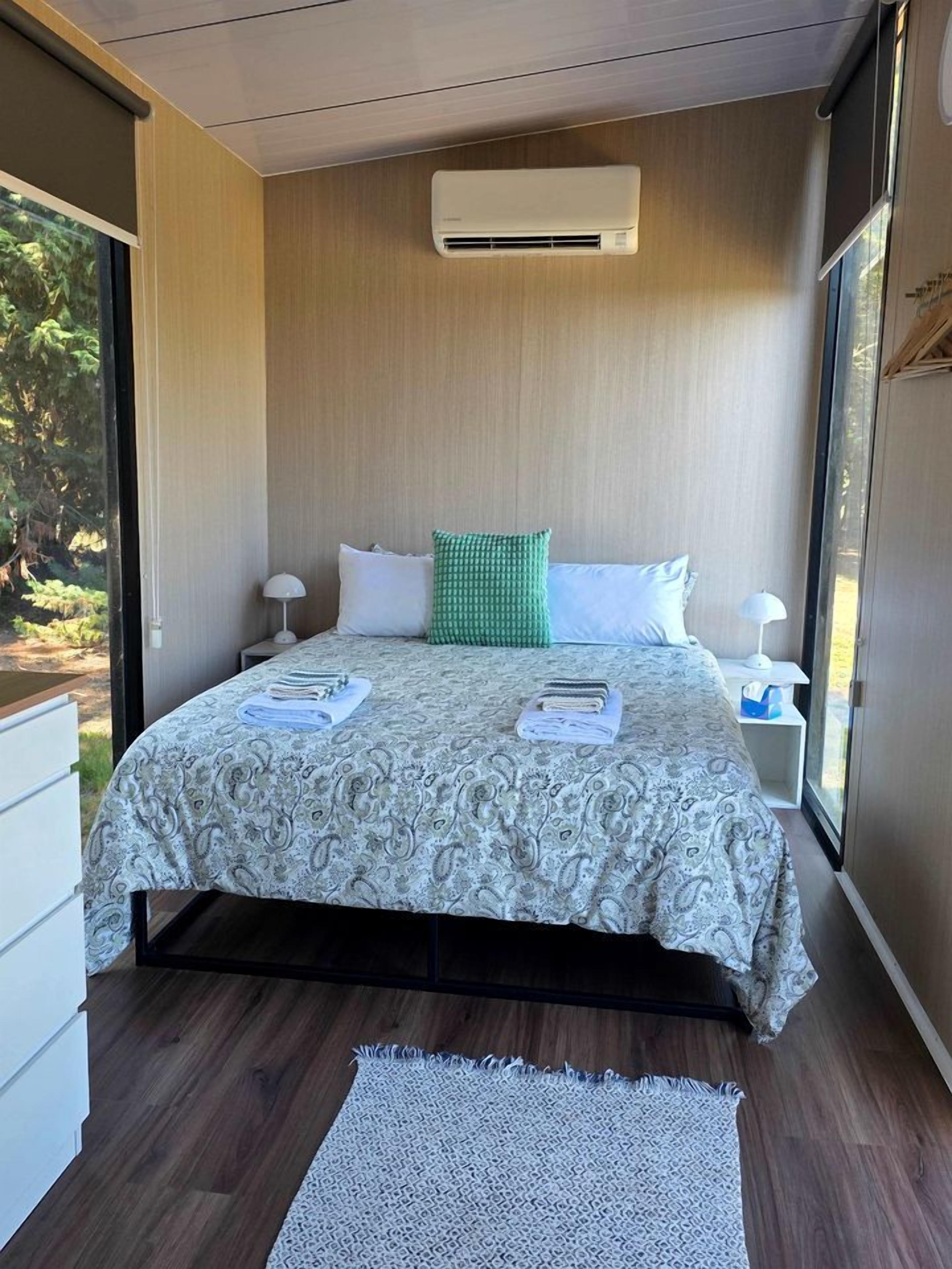 Un dormitorio con cama, mesitas de noche, equipo de aire acondicionado y vistas al exterior.