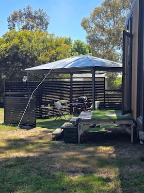 Un área de estar al aire libre cubierta con mesa y sillas, una parrilla y un cerramiento.