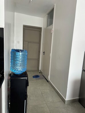 A hallway with a water dispenser, a closed door, and a pair of slippers on the floor. - Cynthia’s Gateway with a Swimming Pool – Stylish & Serene Stay (Nairobi)