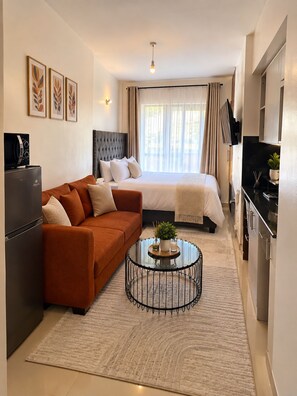 A compact hotel room with a bed, sofa, and kitchenette. - Cynthia’s Gateway with a Swimming Pool – Stylish & Serene Stay (Nairobi)