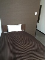 Una cama con colcha a rayas y almohada blanca en una habitación con pared lisa y una puerta.