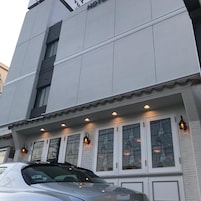 Un hotel con fachada moderna, varios ventanales con detalles decorativos y un coche estacionado frente a él.