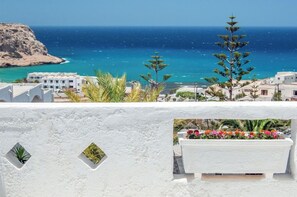 Vista costera con un edificio blanco, un balcón con flores y un mar azul cristalino.