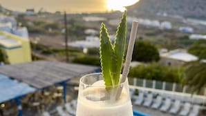 Een cocktailglas met garnering op een balkon met uitzicht op een zwembad en een bergachtig landschap.